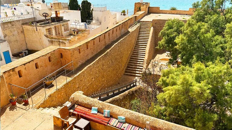 Vue sur la Kasbah de Hammamet et ses remparts surplombant la mer, avec promenade côtière et terrasses.